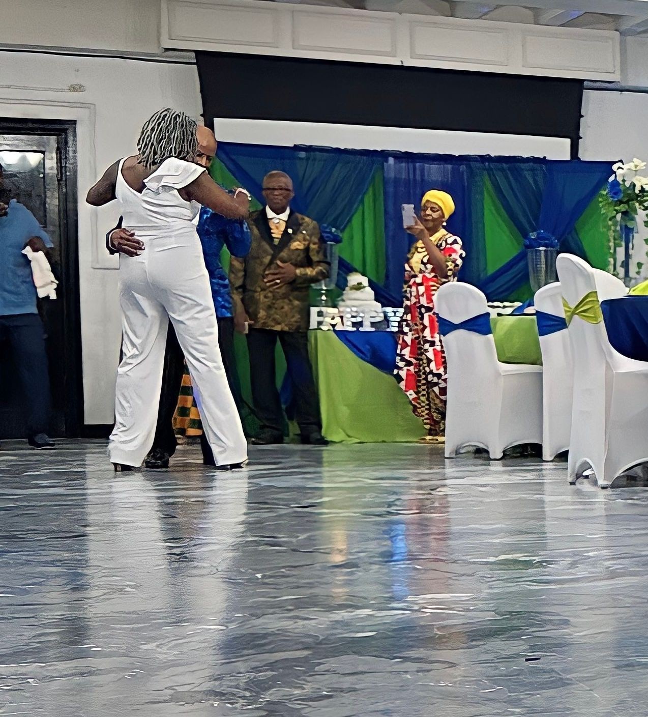 People dancing and celebrating at a decorated indoor event with blue and green-themed decor.